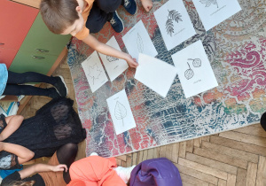 Uczestnicy zajęć świetlicowych oglądają liście różnych drzew przedstawione na obrazkach.