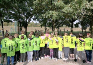Uczniowie klasy 4 ubrani w sportowe koszulki stoją tyłem prezentując numery zawodników i numer szkoły na koszulkach
