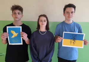Troje uczniów. Dwoje trzyma symbole solidarności z Ukrainą.