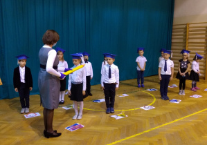 Pani dyrektor pasuje dzieci na uczniów Szkoły Podstawowej nr 113 w Łodzi dotykając dużym ołówkiem prawego ramienia każdego dziecka.