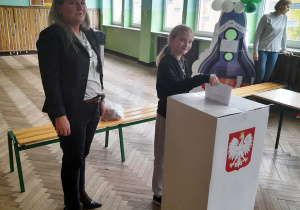 Uczennica wrzuca kartę do głosowania do urny.