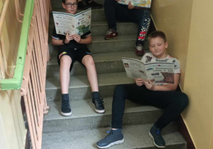 Uczniowie klasy 5b czytają podczas przerwy siedząc na schodach.
