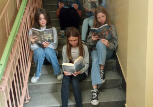 Uczniowie klasy 7a czytają podczas przerwy siedząc na schodach.