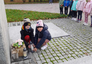 Dwoje uczniów klasy 1b ustawia znicz pod pomnikiem Legionisty.